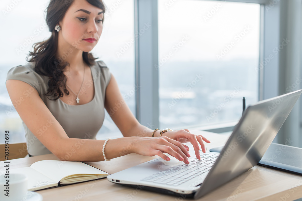 Obraz premium Young businesswoman sitting at work desk, reading and typing new e-mail, using internet on the portable computer.