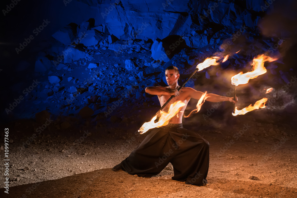 Fototapeta premium Fireshow performance in the desert near the rock illuminated with blue. Motions are blurred