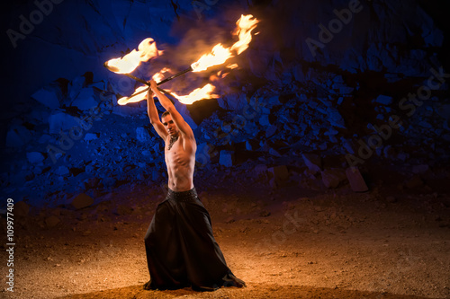 Tableau sur toile Fireshow performance in the desert near the rock illuminated with blue