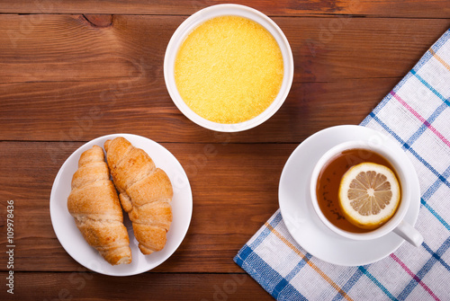 Fototapeta Naklejka Na Ścianę i Meble -  Tea with lemon and honey croissants on a kitchen table.