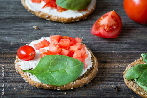 Healthy light snack toast with white cheese, tomato and baby spinach on rustic wooden backdrop. Selective focus, close up