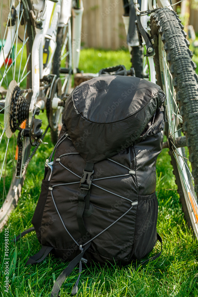 Two bicycles and black Backpack with green outside background, back view