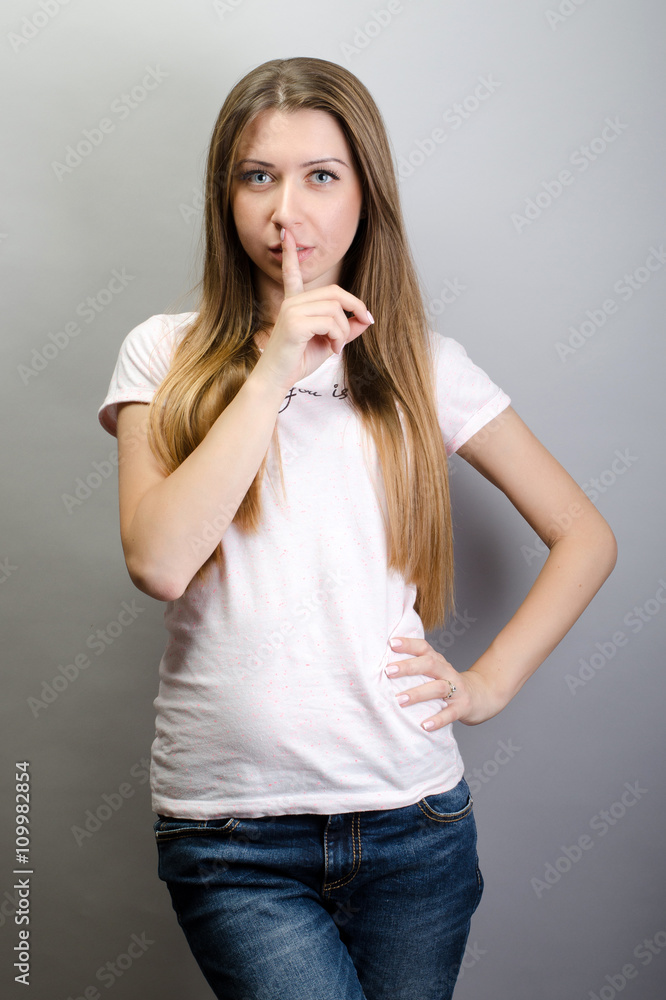 Portrait of young beautiful woman keeping finger on her lips and asking to keep quiet, over grey background Portrait of young beautiful woman keeping finger on her lips and asking to keep quiet, over grey background