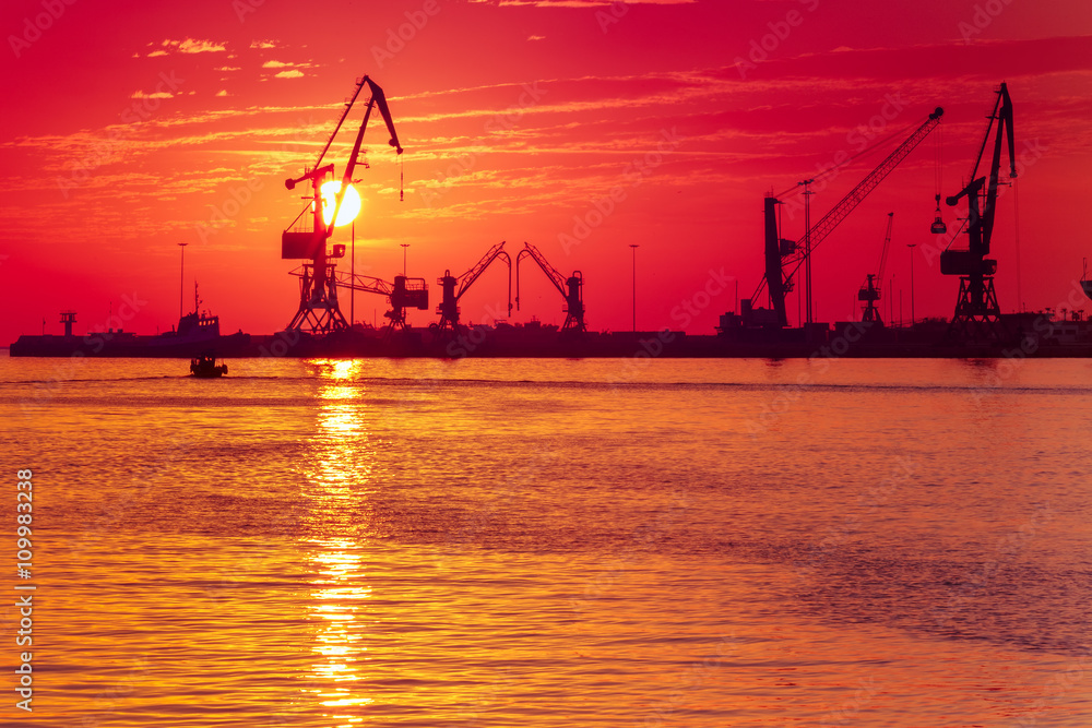 Cranes in sea cargo port of Heraklion on the background of the rising sun, Crete, Greece. 