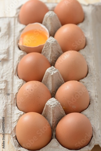 brown eggs in carton with an open egg