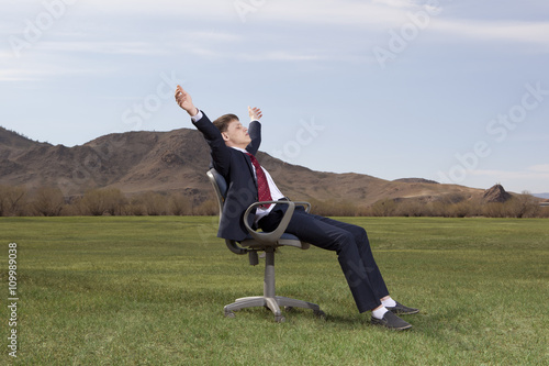 Businessman sitting on chair on green meadow