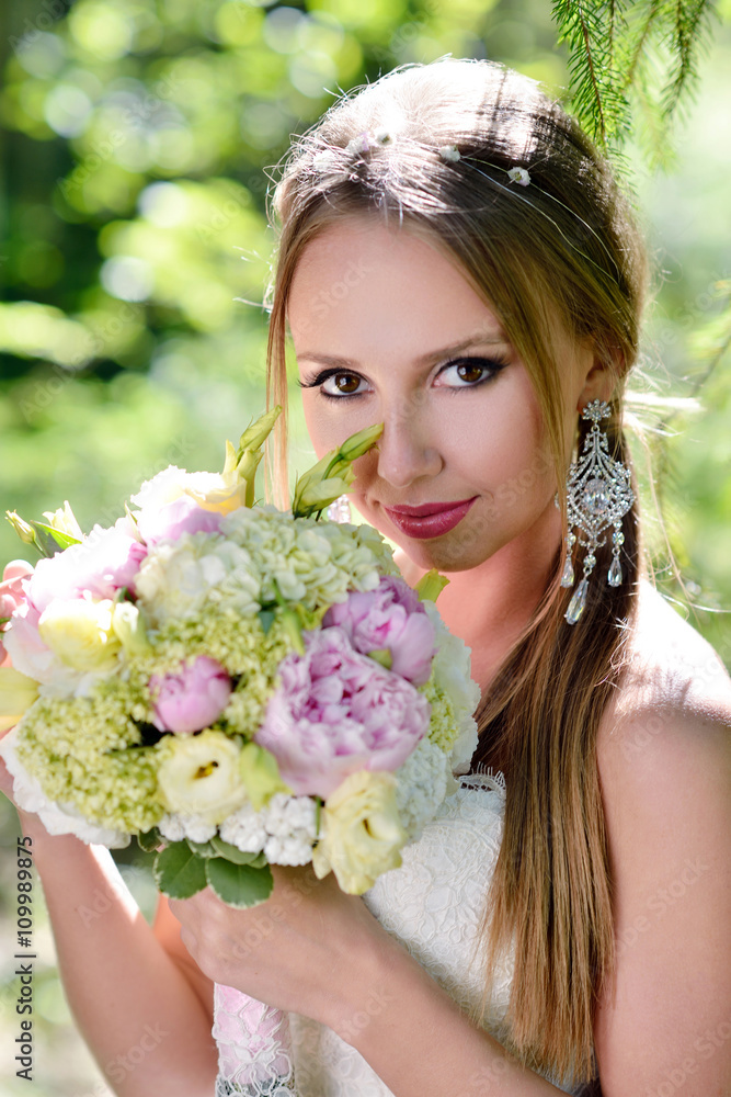 Fototapeta premium Beauty bride in bridal gown with bouquet and lace veil on the nature. Beautiful model girl in a white wedding dress. Female portrait in the park. Woman with hairstyle. Cute lady outdoors