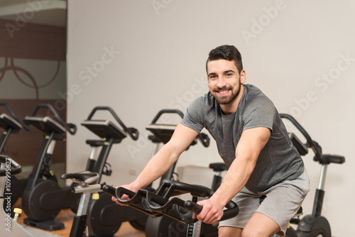 Muscular Man Doing Cycling In Modern Fitness Center