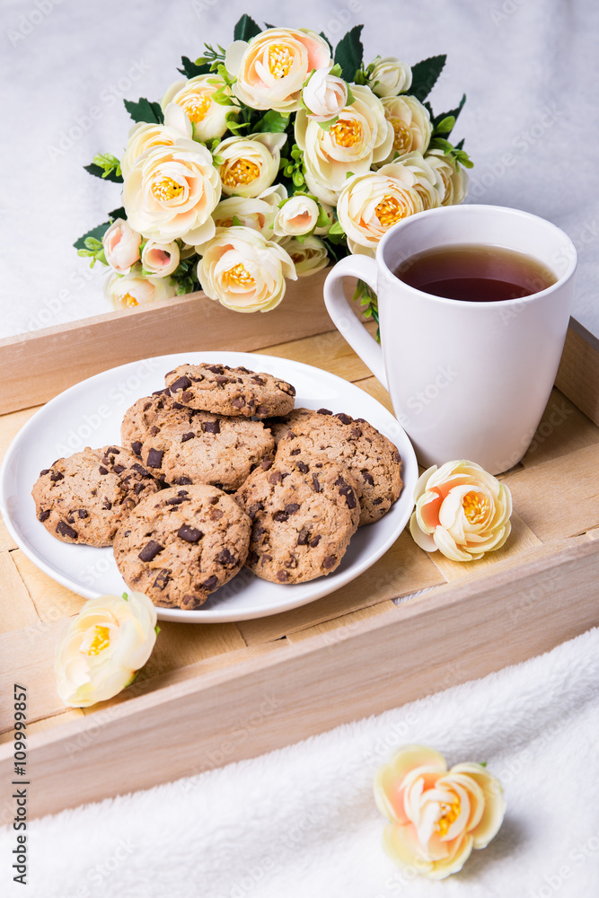 wooden tray with chocolate chip cookies, cup of tea and flowers wooden tray with chocolate chip cookies, cup of tea and flowers