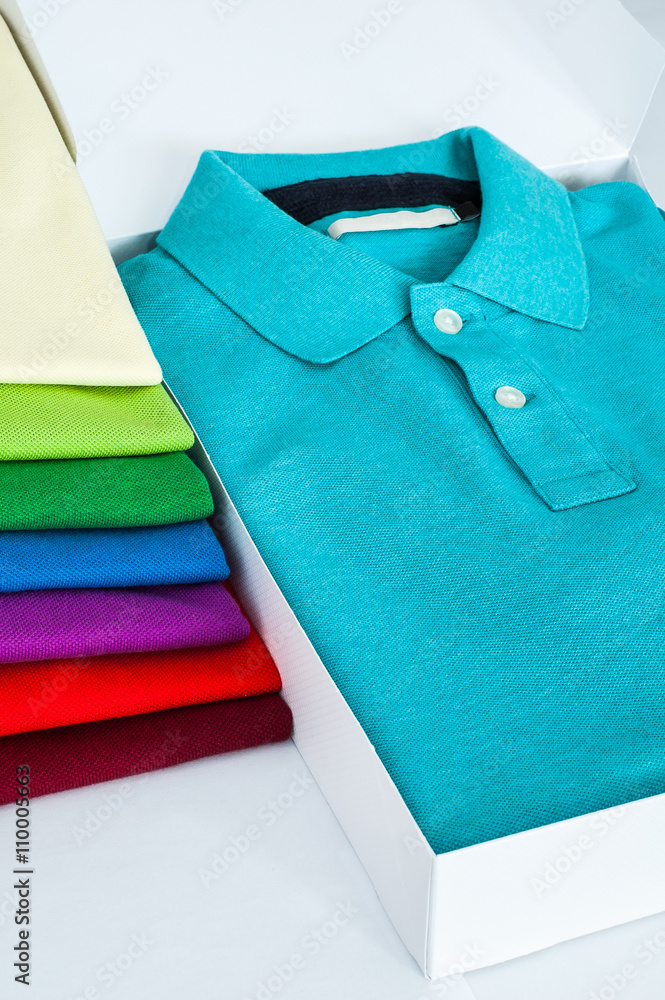 Luxurious fine material 100% cotton polo shirt displayed in a gift box with  a pile of another polo shirts in many different colors. Photos | Adobe Stock