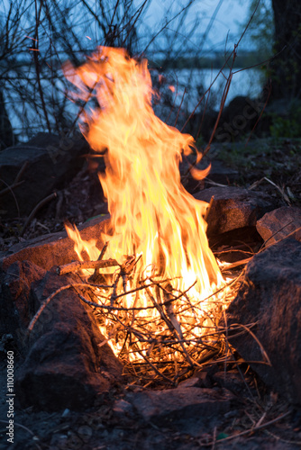 Bonfire between rocks in the wood with lake on the background