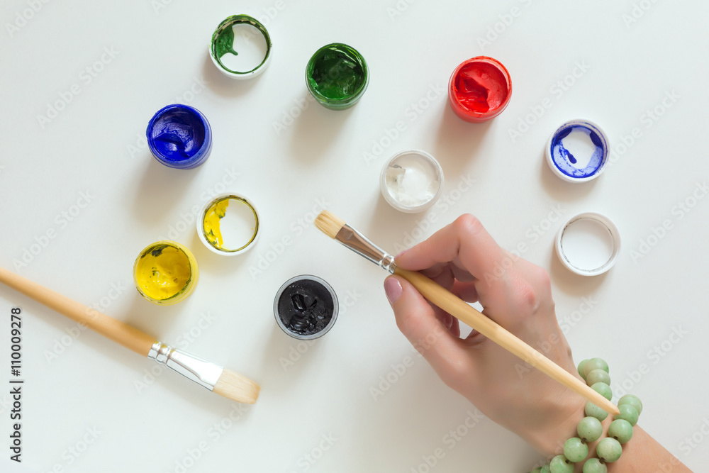 Hand of Artist holding Brush and color Paints on white Table Hand of Artist holding Brush and color Paints on white Table