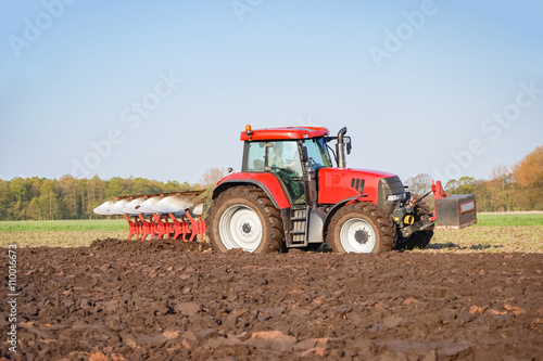 Ackerbau  roter Traktor mit rotem Pflug bei der Bodenbearbeitung