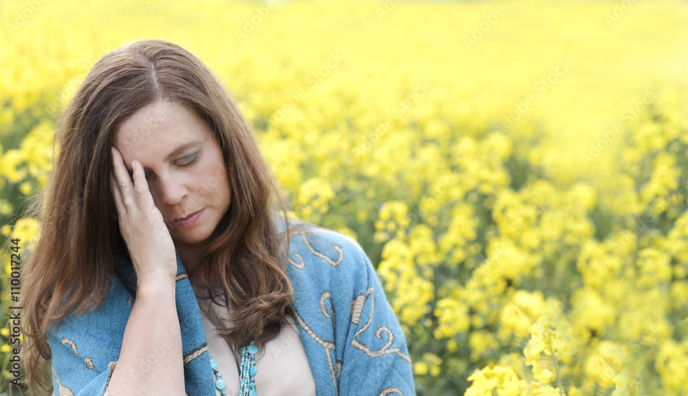 Depressive ältere Frau mit Händen vor dem Gesicht im Rapsfeld in der Natur Depressive ältere Frau mit Händen vor dem Gesicht im Rapsfeld in der Natur