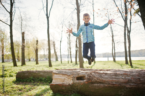 Little fun boy jump froom tree stump at park