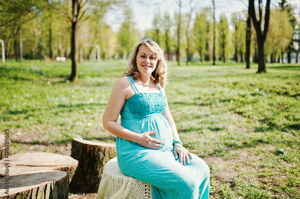 Happy pregnant woman dressed in a turquoise dress sitting on a s Happy pregnant woman dressed in a turquoise dress sitting on a s