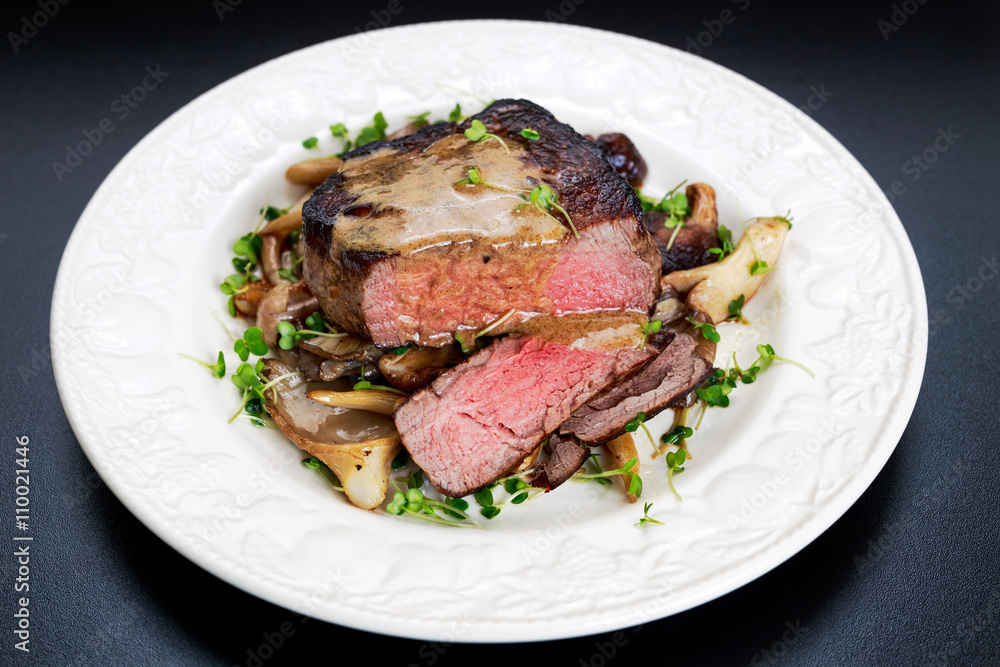 Tasty Beef Mignon steak with mushrooms and herbs on plate.