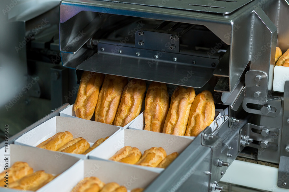 Boxes with pastry on conveyor. Device putting eclairs into boxes. Automated production of sweet food. High sugar content food. Boxes with pastry on conveyor. Device putting eclairs into boxes. Automated production of sweet food. High sugar content food.