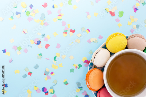 Colorful macaroons with cup of tea on confetti background
