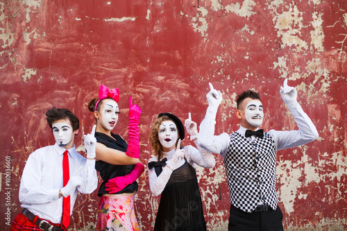 Four mimes point to the top on a red wall.