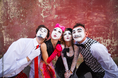 Four mimes cute pose in front of a red wall.