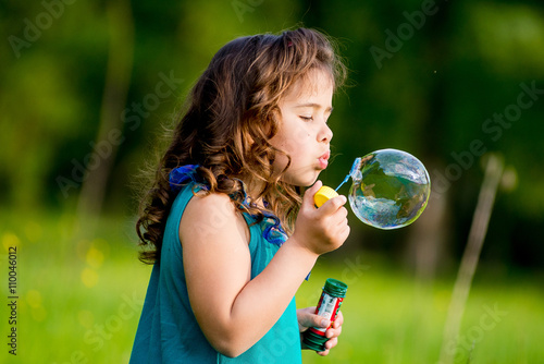 Little girls blow bubbles sitting on the grass