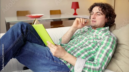 Man lying on the sofa and writing something in the notebook
