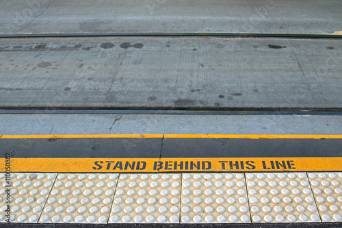 Closeup of tramway with yellow signage “STAND BEHIND THIS LINE” on concrete road at the tram stop in Melbourne, Australia