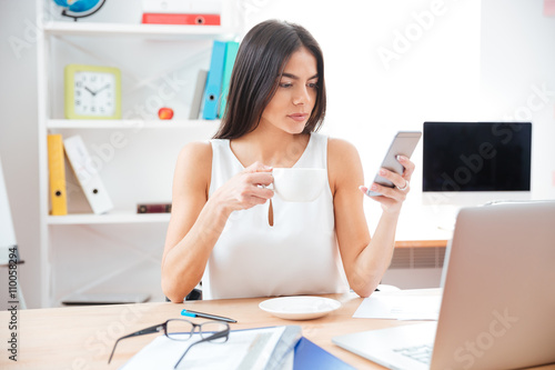 Businesswoman drinking coffee and using smartphone