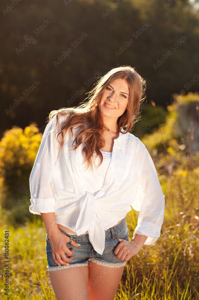 Smiling young woman 25 year old wearing white shirt and denim shorts outdoors. Looking at camera. 20s. Smiling young woman 25 year old wearing white shirt and denim shorts outdoors. Looking at camera. 20s.