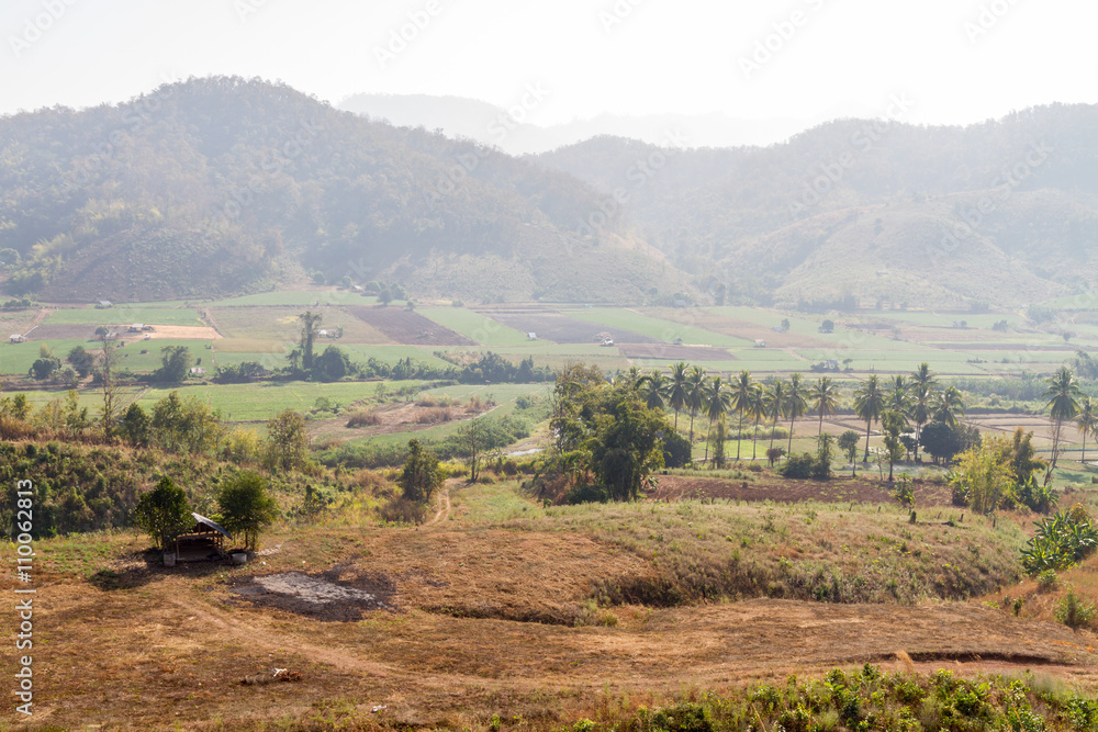 Naklejka premium Countryside farm field surrounded by mountain with haze