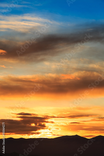 Sun behind dark mountain silhouettes, with colorful sky and clouds