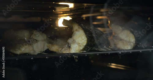 Closeup shot of fish pieces cooking in the hot oven. Someone is opening the oven door and checking if it is done. photo