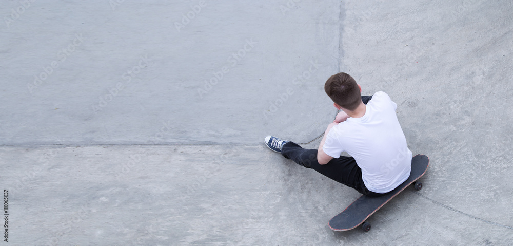 Young man in t-shirt and jeans sitting on skateboard Young man in t-shirt and jeans sitting on skateboard