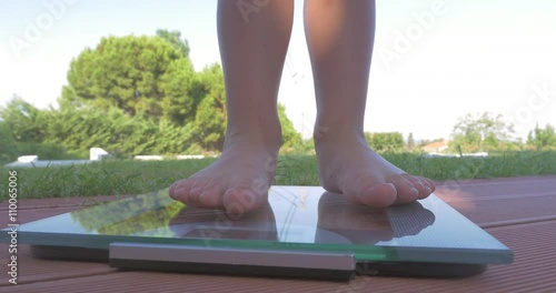 Close-up shot of little child feet standing on electronic scales outdoor. Scene with green trees and grass in background photo