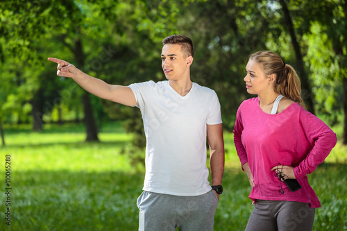 Fototapeta Naklejka Na Ścianę i Meble -  Running couple talking in the park. Man shows the path where they will run.