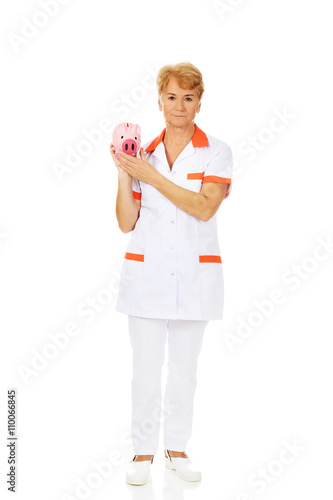Smile elderly female doctor or nurse holding piggybank