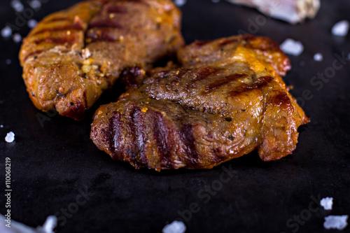 Roasted meat grilled with spices and garlic on black wooden background