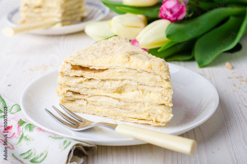 Slice of napoleon cake with tulips on white vintage background. Selective focus Slice of napoleon cake with tulips on white vintage background. Selective focus