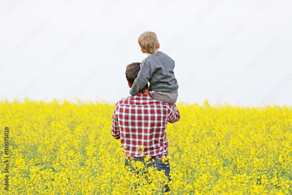 man with a child in a a blossom yellow field