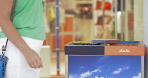 Woman throwing bottle into the container for plastic litter in shopping center. Waste sorting photo