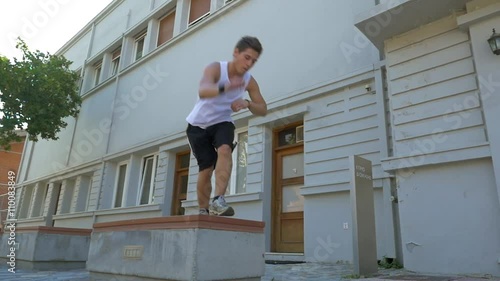 Slow motion steadicam shot of a young sportsman taking exercise in extreme sport. He doing somersaults while jumping from stone street bench photo