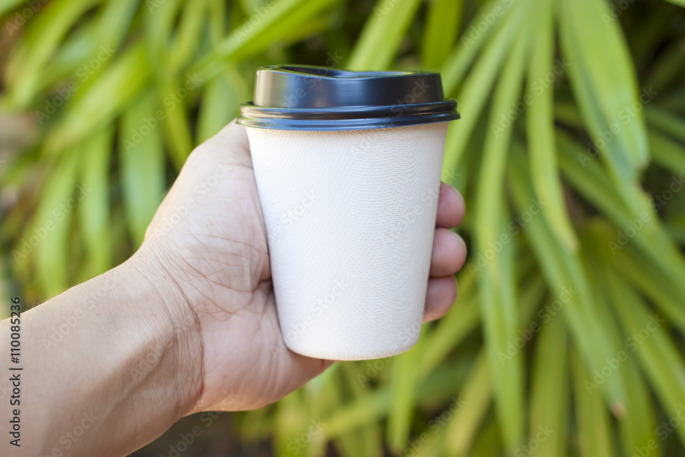 Hand holding paper coffee cup with green nature background Hand holding paper coffee cup with green nature background