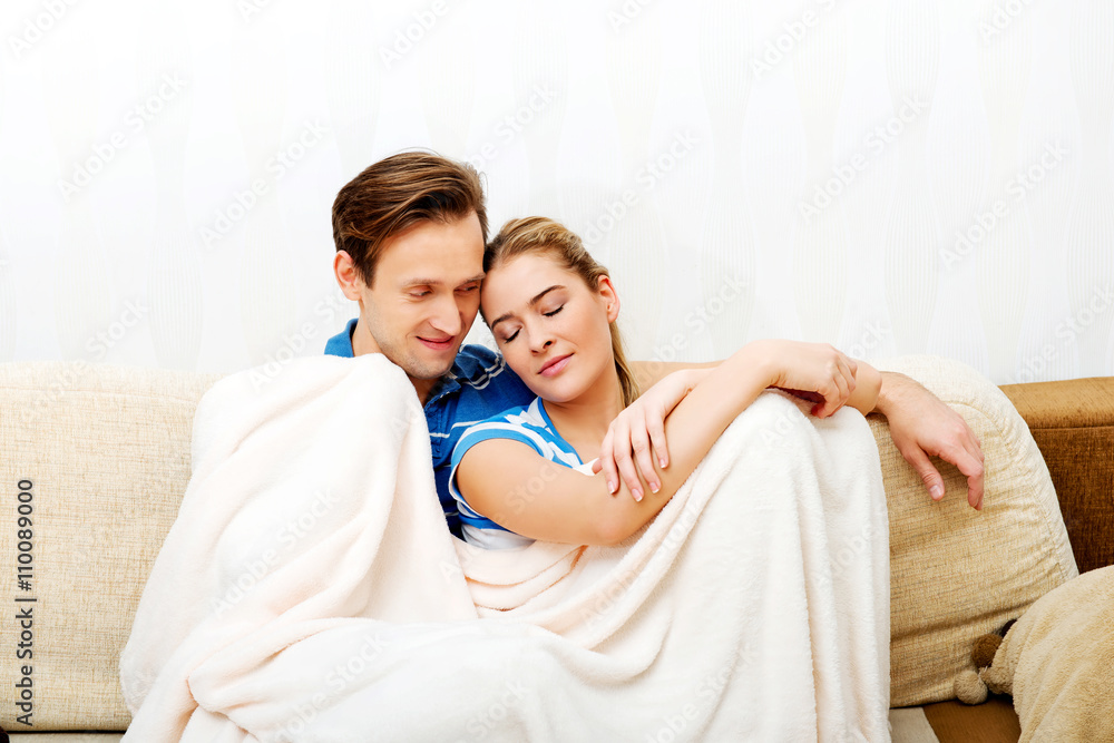 Smiling loving couple sitting on couch with blanket Smiling loving couple sitting on couch with blanket