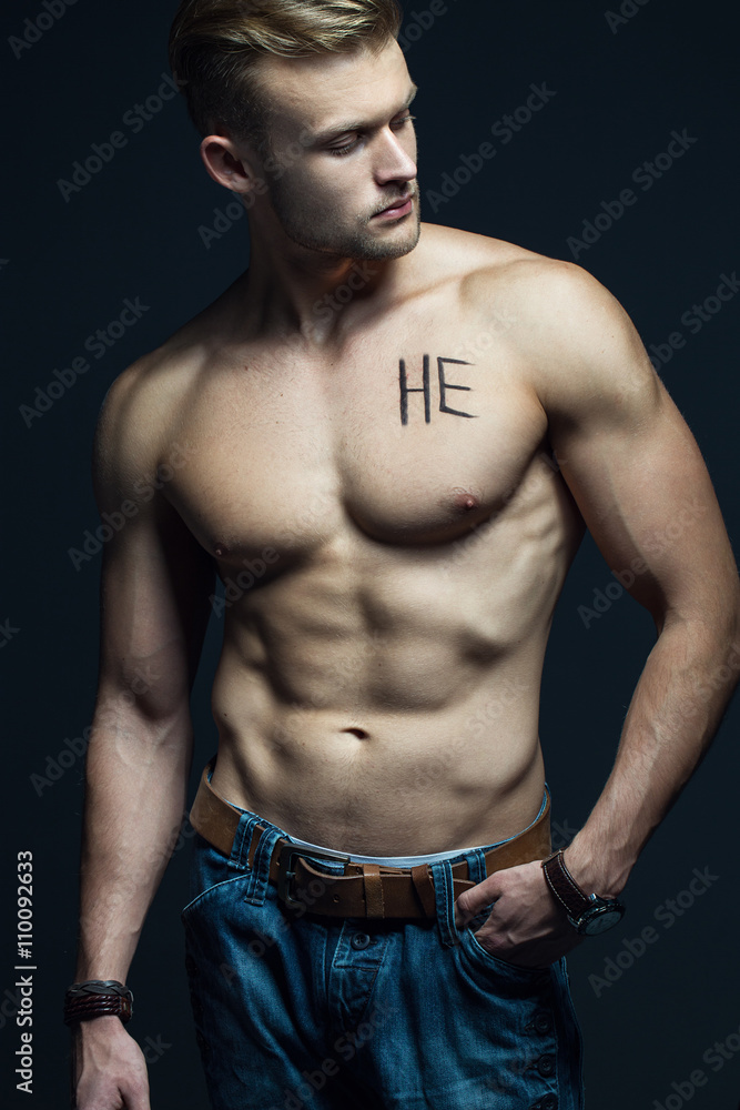 Fototapeta premium Handsome muscular male model with intense glance posing over grey background. Perfect body with the inscription 