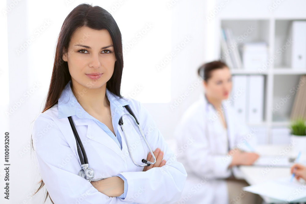 Brunette female doctor on the background of colleagues talking to each other in hospital Brunette female doctor on the background of colleagues talking to each other in hospital