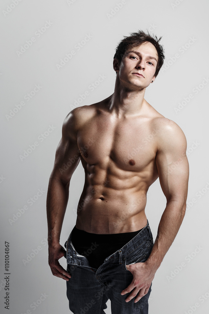 Muscular male model bodybuilder with unbuttoned jeans. Studio shot on gray background. Fitness MODEL. Great for commercial. Ideal fitness body with six pack, perfect abs, shoulders. 