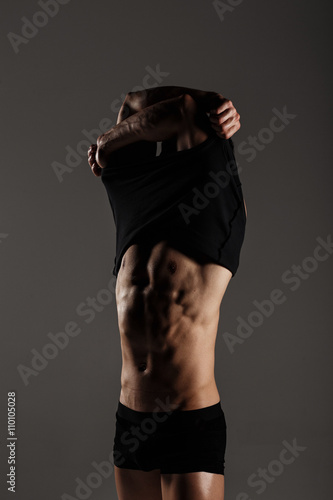 Muscular male model bodybuilder after training remove t-shirt. Studio shot on gray background. Great for commercial. Ideal fitness body with six pack, perfect abs, shoulders, biceps, triceps, chest photo