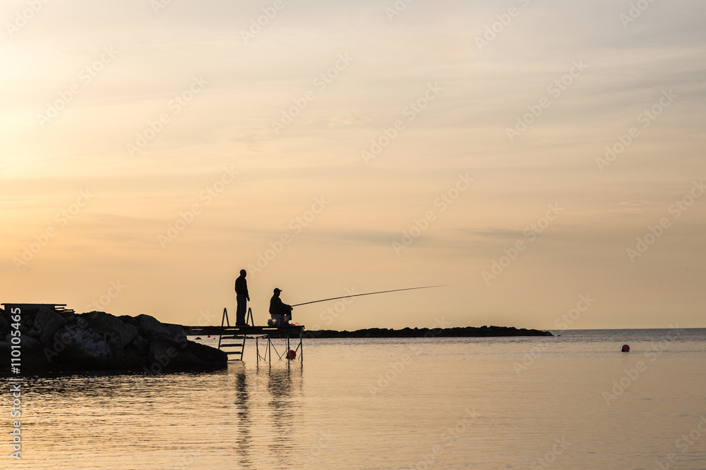 silhouettes of two fishermen on a background of sunrise