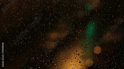 Luces de colores desenfocadas de letreros luminosos y de coches,  a traves de un cristal de ventana con gotas de lluvia y por la noche